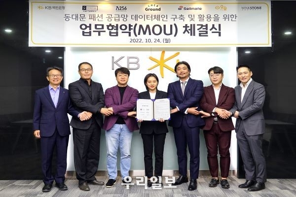 지난 24일 서울시 영등포구 KB국민은행 여의도 IT센터에서 열린 동대문 패션 공급망 데이터체인 구축 및 활용을 위한 업무협약식에서 (왼쪽부터) 윤진수 KB국민은행 테크그룹 대표, 이한수 굿티어 대표, 박재현 람다256 대표, 이연 쉐어그라운드 대표, 서원준 셀메이트 대표, 조형일 위아더 대표, 권오형 윙크스톤파트너스 대표가 기념촬영을 하고 있다.
